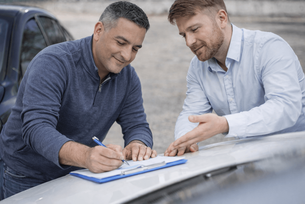 Zwei Männer stehen neben einem Auto, einer unterschreibt einen Kostenvoranschlag auf einem Klemmbrett, während der andere gestikuliert und erklärt